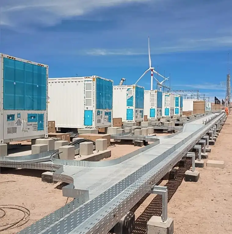 Contenedores BESS y bandejas de cables en obra, con aerogeneradores al fondo
